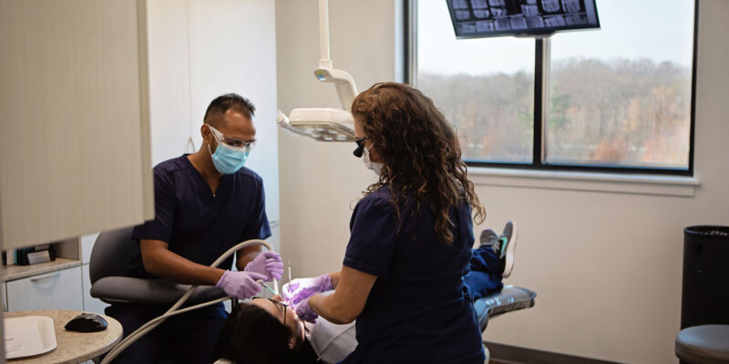 Dentist and dental assistant performing a procedure on a patient in a clinic, with an X-ray monitor overhead