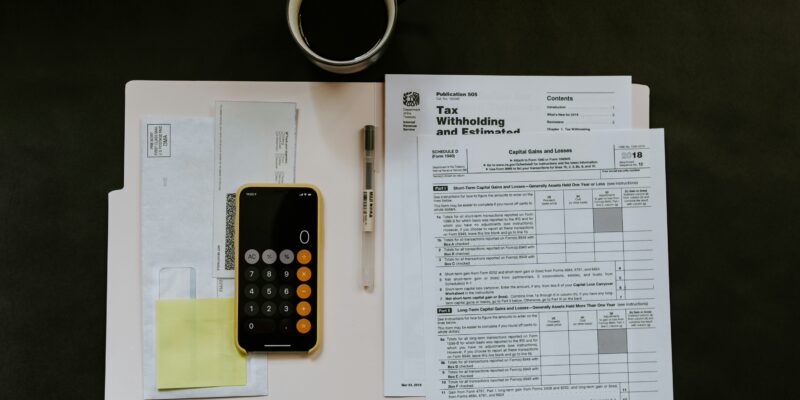 Top-down view of a desk with a cup of black coffee, a calculator, pen, sticky notes, and tax documents spread on white folders.