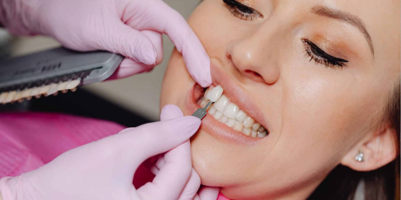 Dentist wearing pink gloves applying a whitening tray to a woman's upper teeth during a dental procedure.