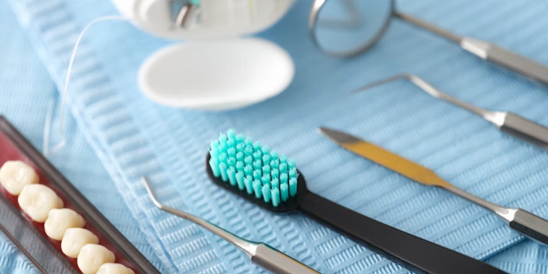 Dental care tools on a blue surface: turquoise toothbrush, mirror, dental picks, and a denture model.