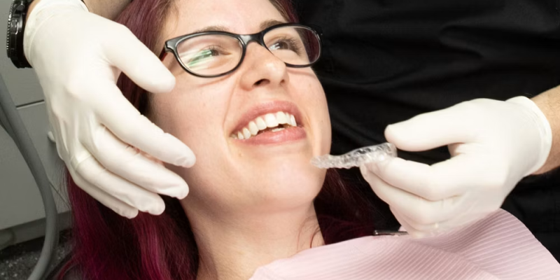 Woman in a dental chair smiles as a clinician places a clear orthodontic aligner into her mouth wearing gloves? (informative)